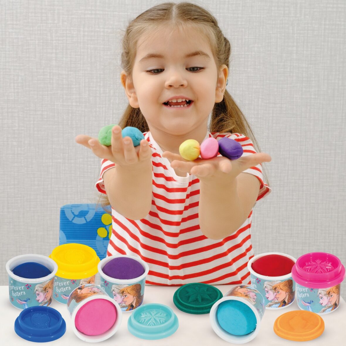 little smiling baby girl in striped T-shirt plays with colored plasticine, play dough at home