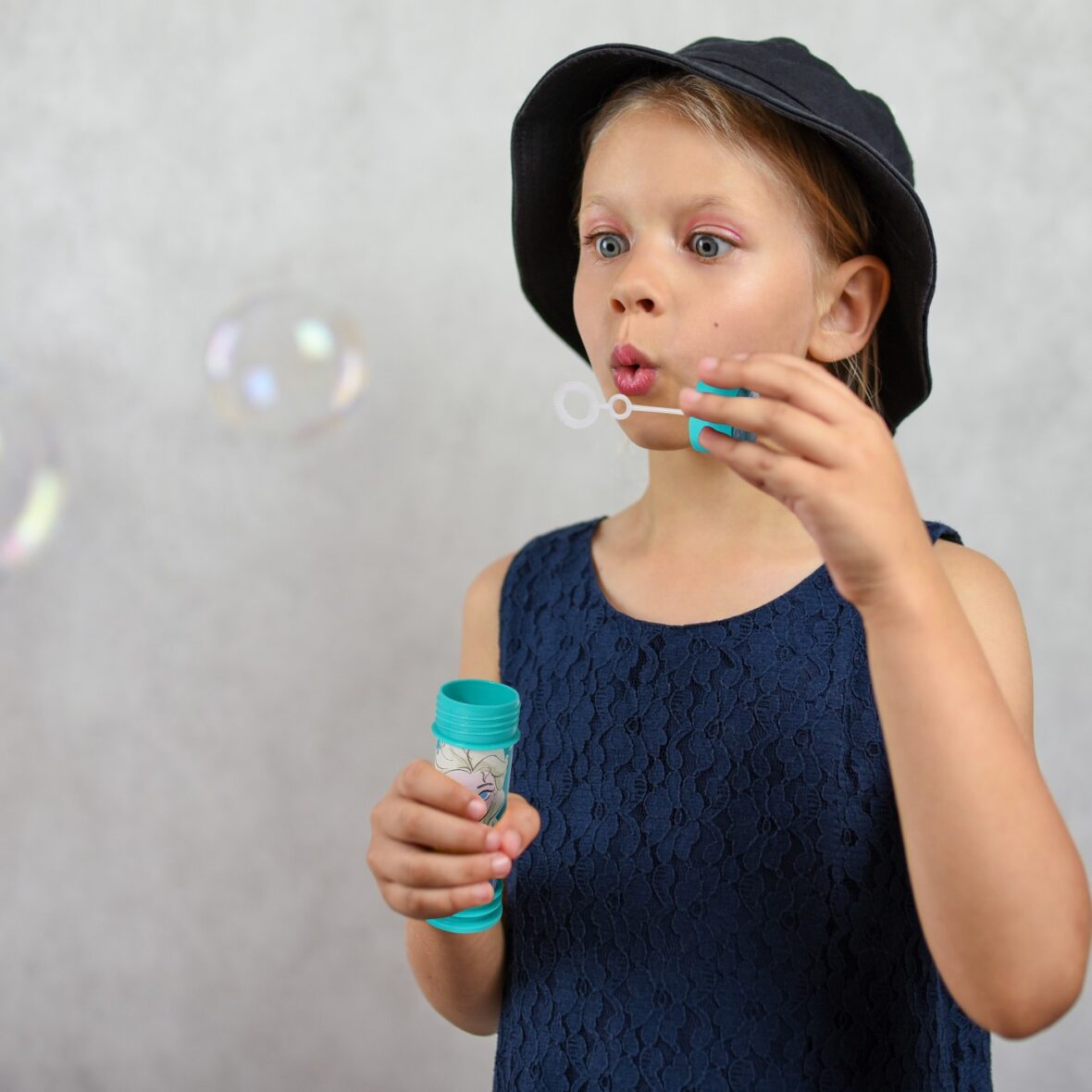 Young girl in a hat and dress blows bubbles