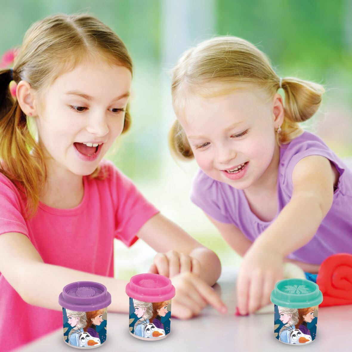 Two cute little sisters having fun together with modeling clay at a daycare. Creative kids molding at home. Children play with plasticine or dough.